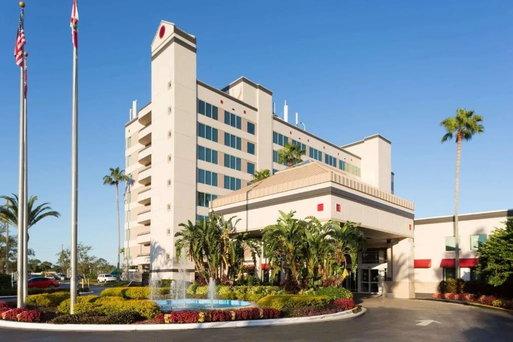 Paseo de entrada con banderas, fuente y la torre del hotel en Ramada by Wyndham Kissimmee Gateway