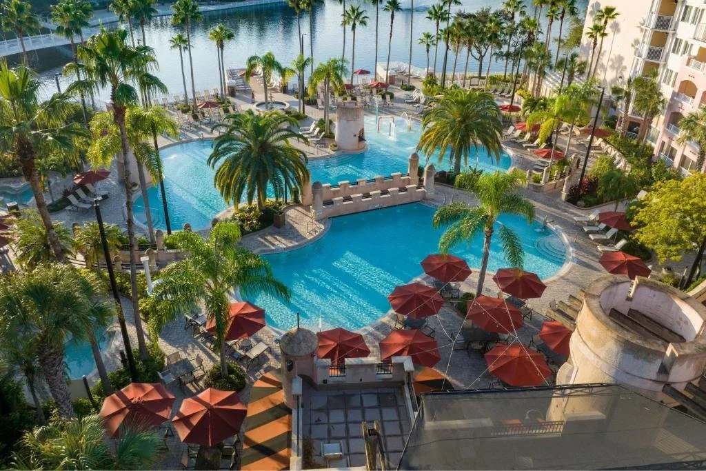 Vista aérea de piscinas bordeadas de palmeras, sombrillas rojas y lago en el Marriott's Grande Vista