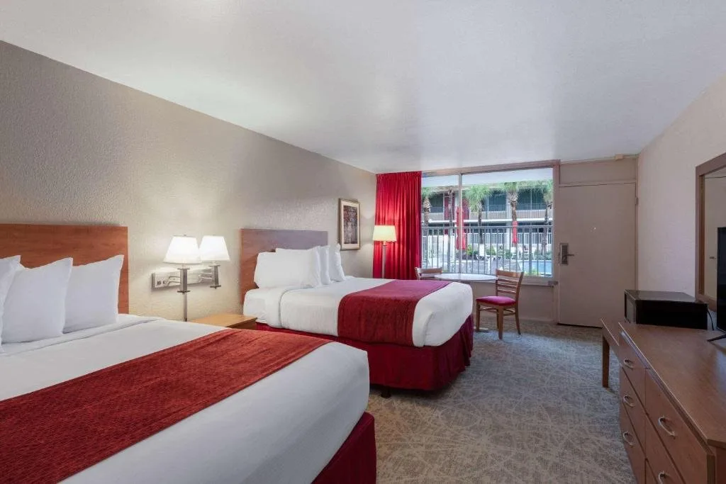 Dos camas con bufandas rojas y una ventana al Courtyard en Ramada by Wyndham Kissimmee Gateway