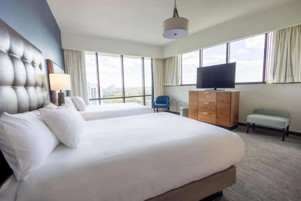 Dos camas junto a las ventanas del piso al techo con vistas a las copas de los árboles en Drury Plaza Hotel Orlando