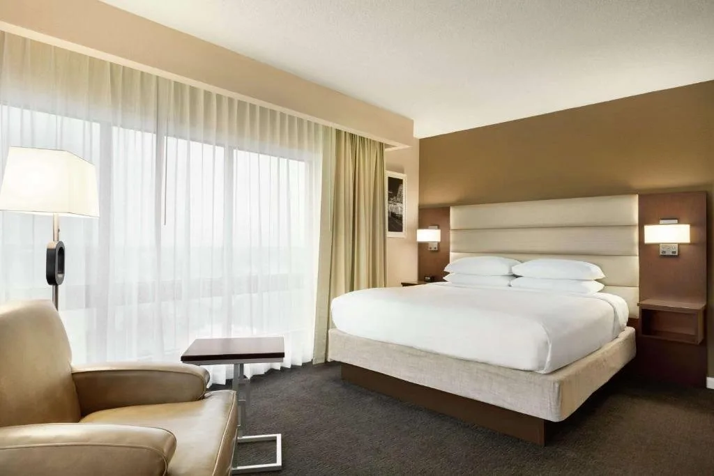 Cama king, sill&oacute;n bronceado y l&aacute;mpara de pie con ventanas con cortinas en DoubleTree by Hilton Orlando Downtown