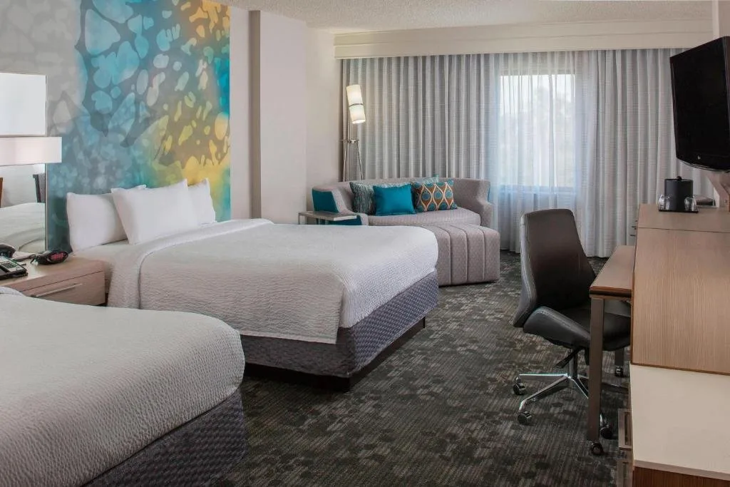 Dos camas, pared de acento colorido y sofá en una habitación Courtyard by Marriott Lake Buena Vista
