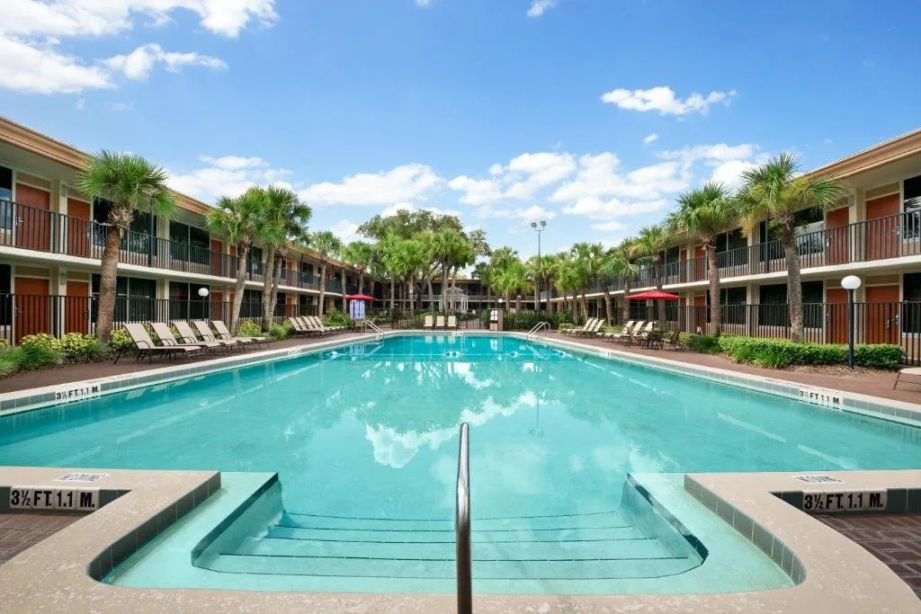 Gran piscina en el Courtyard bordeada de palmeras y tumbonas en Ramada by Wyndham Kissimmee Gateway