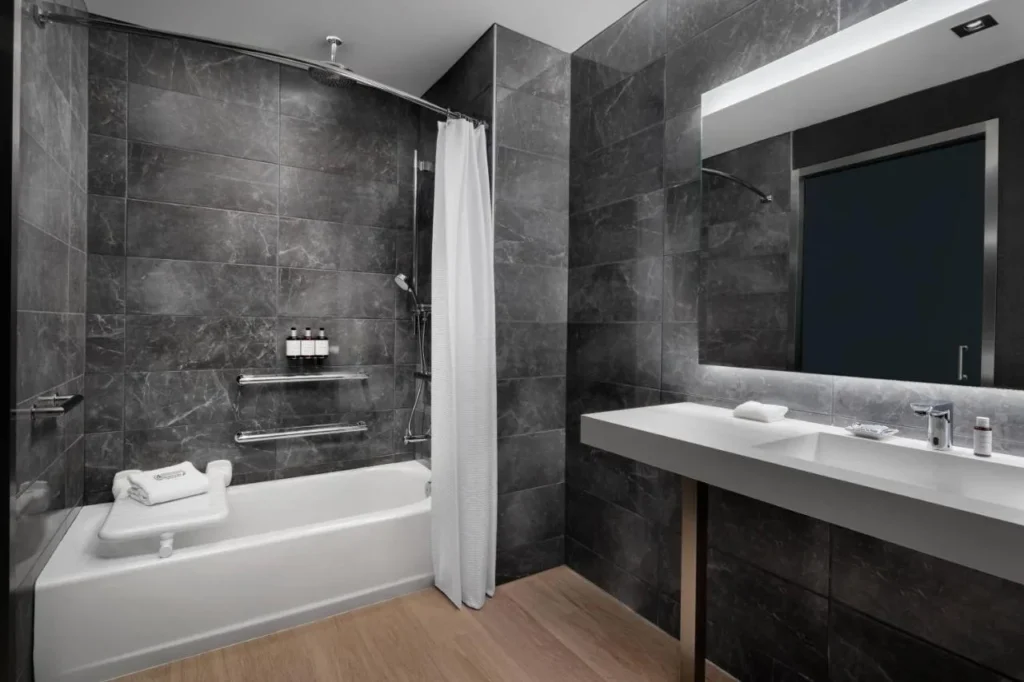 Baño accesible con bañera, barras de sujeción y banco de transferencia en AC Hotel Orlando Downtown