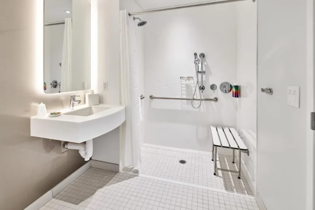 Baño accesible con ducha a ras de suelo, banco de ducha y barra de agarre en Universal Terra Luna Resort