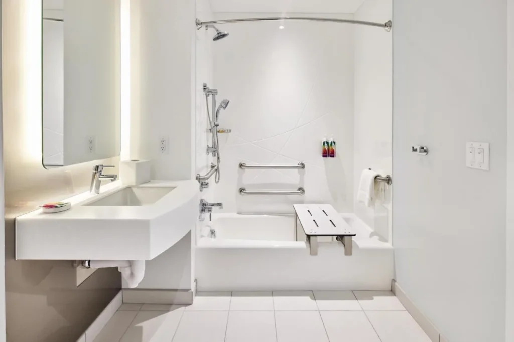 Baño accesible con barras de apoyo, un banco de bañera y ducha de mano en Universal Terra Luna Resort