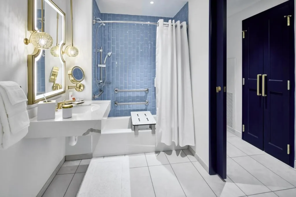 Baño accesible con barras de apoyo, banco de bañera y azulejo en el Universal Helios Grand Hotel