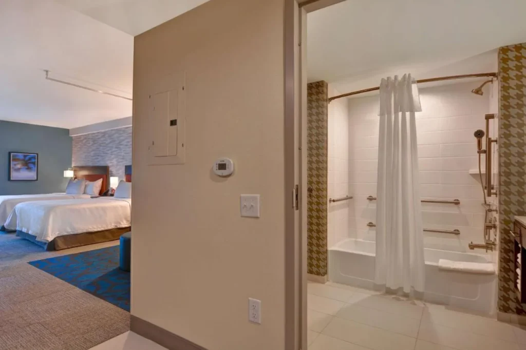 Bañera accesible con barras de apoyo junto a un estudio de dos camas queen en Home2 Suites Flamingo Crossings