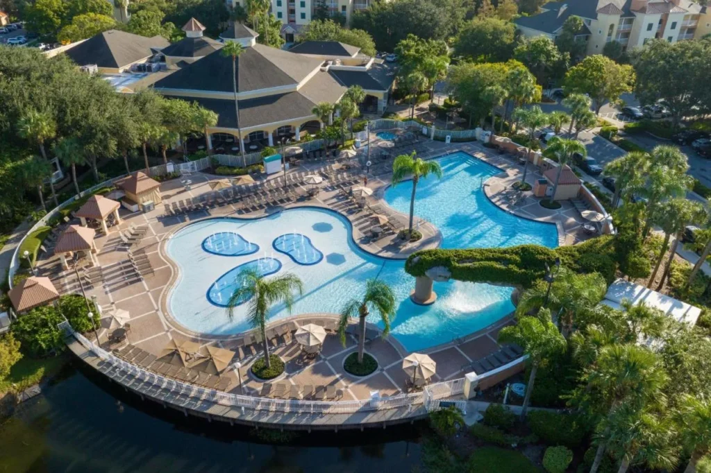 Vista aérea de una piscina de forma libre con chorros de salpicaduras, cabañas y lago en Sheraton Vistana Resort