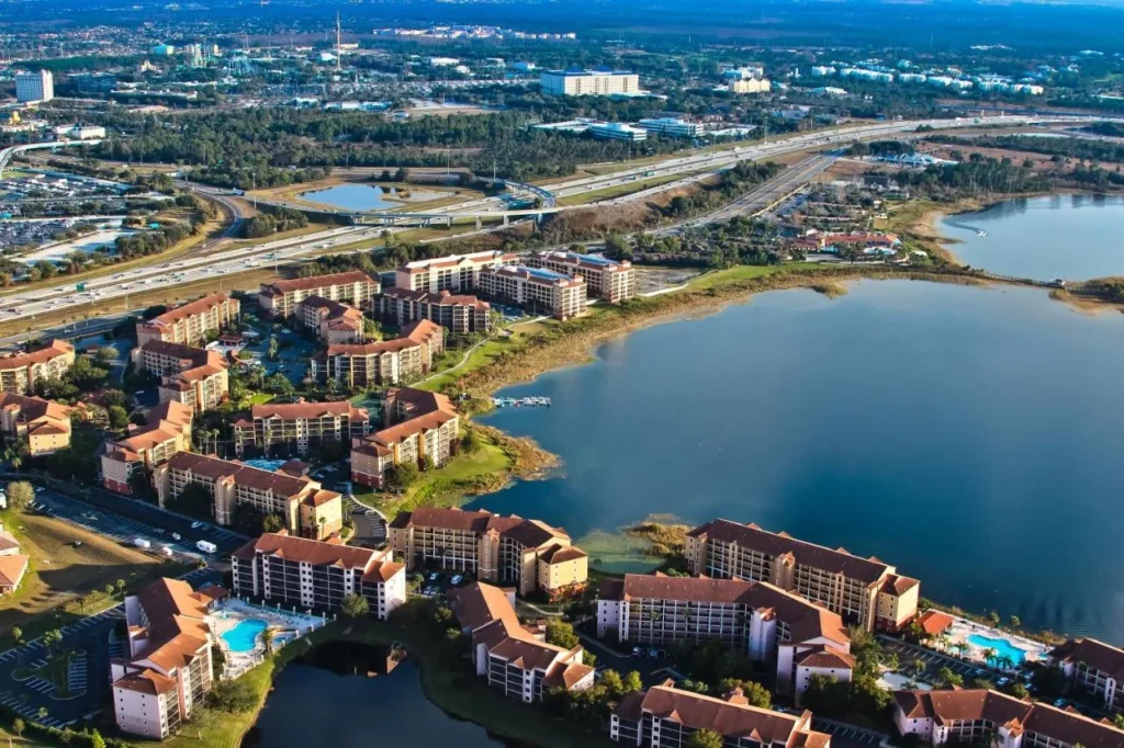 Vista aérea de los edificios y piscinas de la villa Westgate Lakes Resort junto a un gran lago, con una carretera detrás