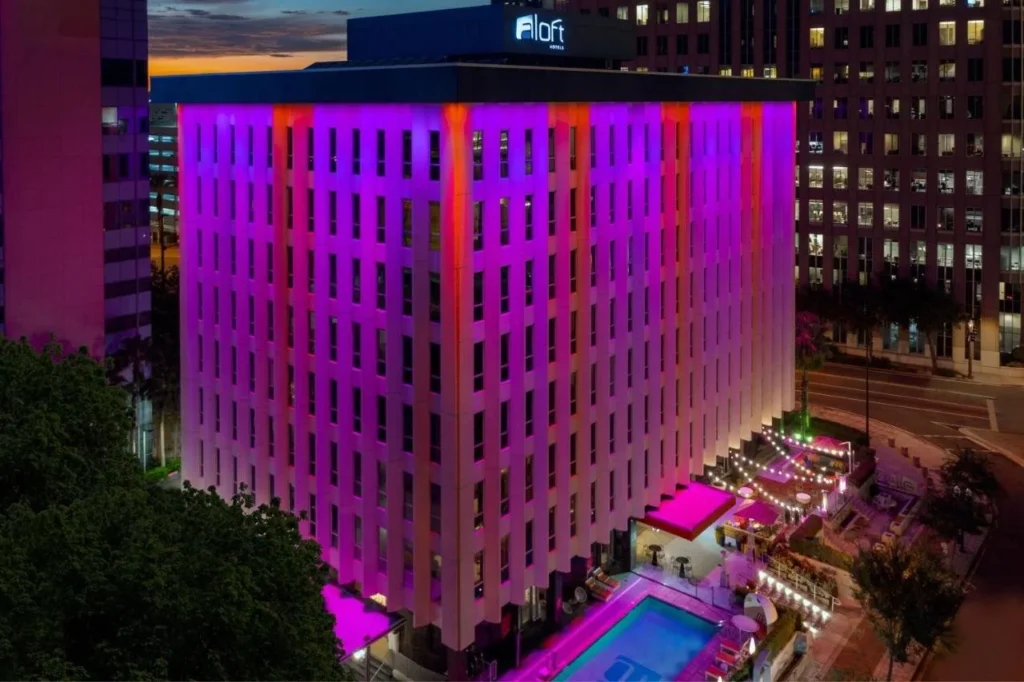 Aloft Orlando Downtown iluminado en rosa y púrpura al atardecer, con su piscina al aire libre a continuación