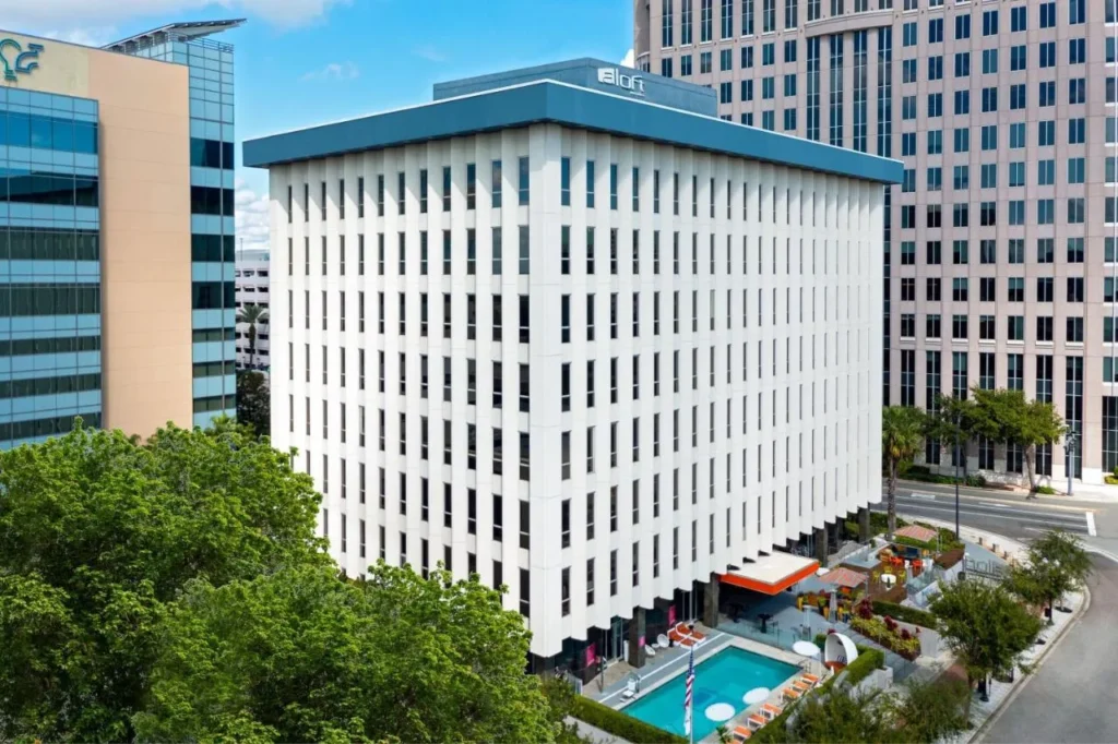 Aloft Orlando Downtown torre blanca con su piscina al aire libre y esquina de la calle bordeada de palmeras