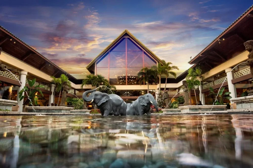 Courtyard de llegada con fuente de elefante y vestíbulo a dos aguas en Loews Royal Pacific Resort al atardecer
