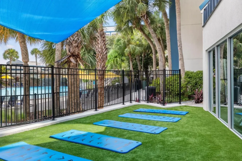 Artificial-grass lawn with exercise mats beside the fenced pool at Delta Hotels Orlando Celebration