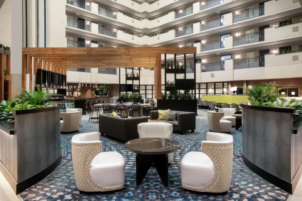 Atrium lounge with armchairs and planters under tiered balconies at Embassy Suites Orlando Airport