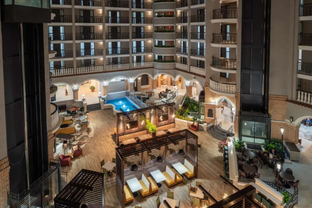 Atrio de Embassy Suites Orlando North con balcones escalonados, asientos en el sal&oacute;n y una fuente iluminada