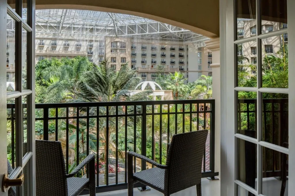 Balcón con dos sillas con vistas al atrio de cristal lleno de palmeras en Gaylord Palms Resort