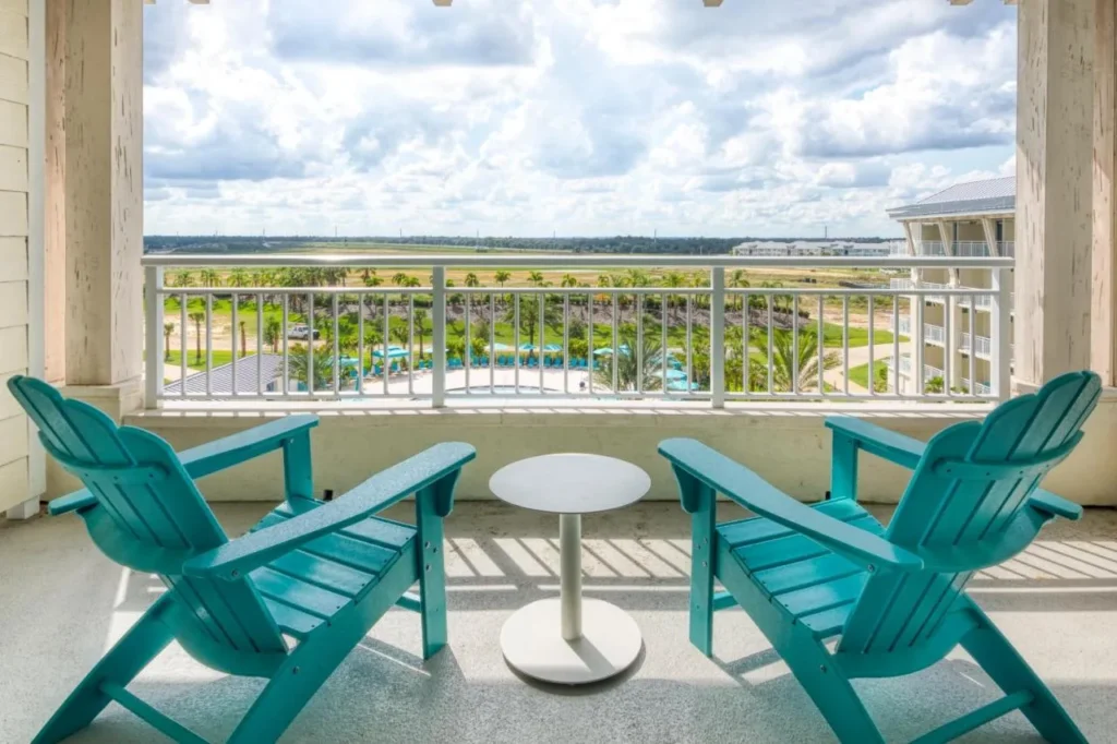 Balcón con dos sillas Adirondack verde azulado con vistas a la terraza de la piscina en Margaritaville Resort Orlando