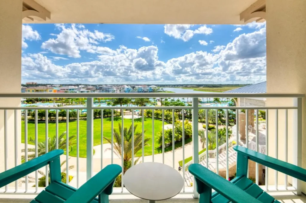 Balcony with two teal chairs overlooking a lawn, pools and cottages at Margaritaville Resort Orlando