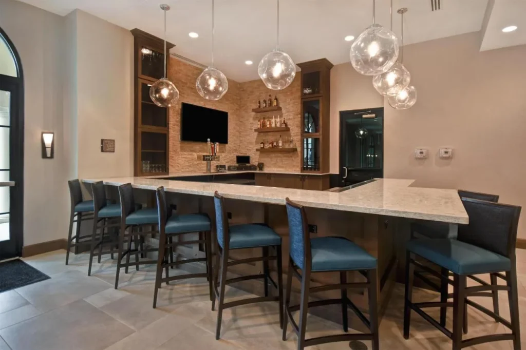 Bar counter with blue stools, TV and glass pendant lights at Homewood Suites Flamingo Crossings