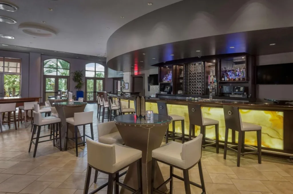 Bar con mostrador de piedra retroiluminado y mesas altas en Wyndham Grand Orlando Bonnet Creek