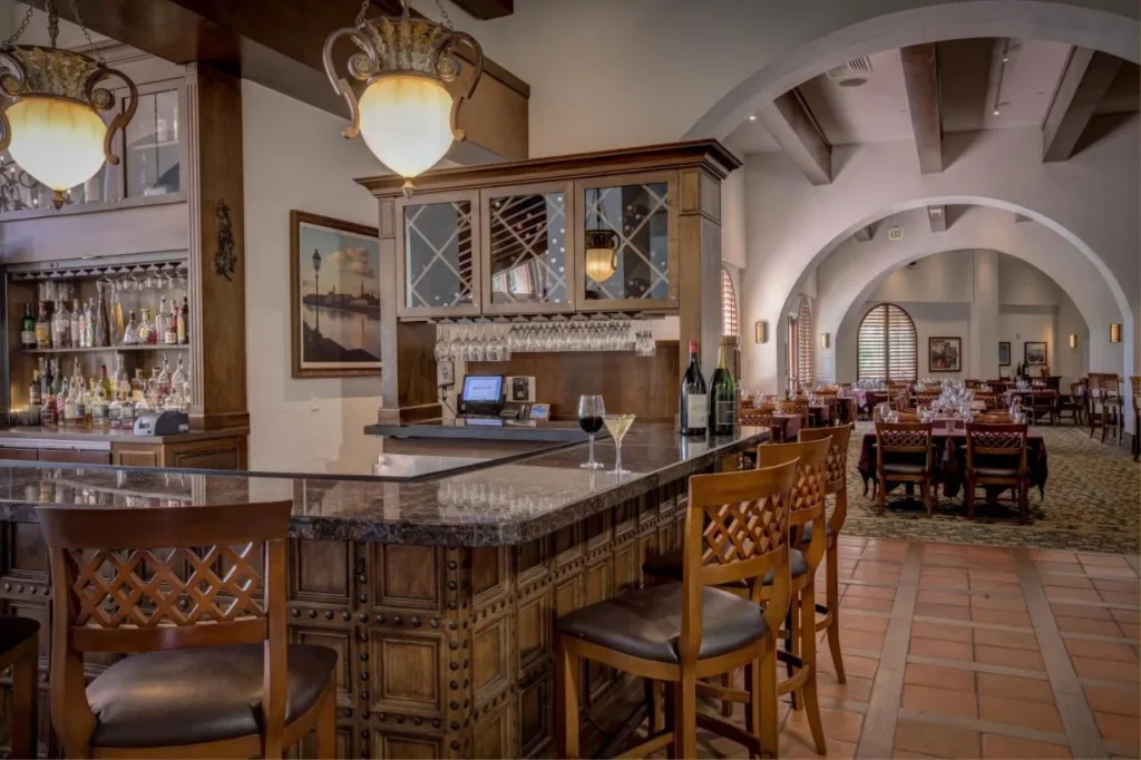 Bar with granite counter and wooden stools beside an arched dining room at Rosen Shingle Creek