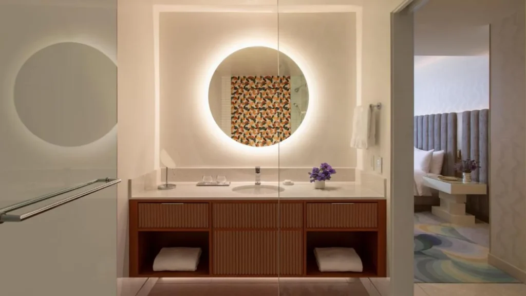 Vanidad del ba&ntilde;o con un espejo redondo retroiluminado y estantes de toalla abiertos en Lake Nona Wave Hotel
