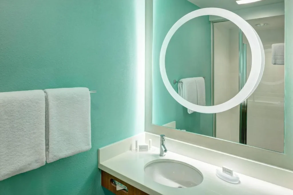 Bathroom vanity with a round lighted mirror and teal walls at SpringHill Suites Orlando at SeaWorld