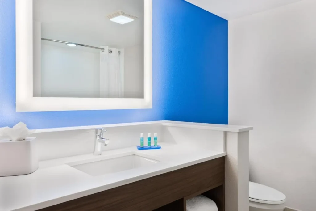 Bathroom vanity with lit mirror and blue accent wall at Holiday Inn Express Nearest Universal