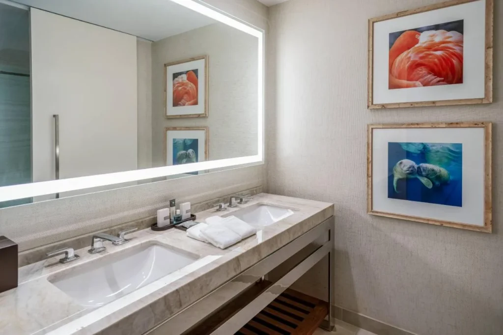 Cuarto de ba&ntilde;o con tocador doble, espejo iluminado y estampados de flamencos y manat&iacute; en Gaylord Palms Resort