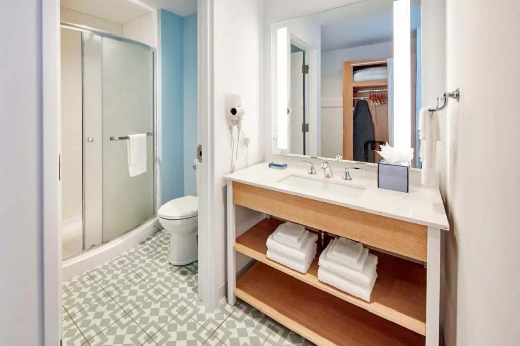 Cuarto de baño con un espejo iluminado, tocador de plataforma abierta y ducha de cristal en Dockside Inn and Suites