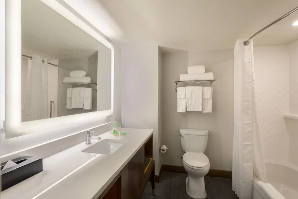 Cuarto de baño con espejo iluminado, tocador largo y bañera en Holiday Inn & Suites Orlando SW