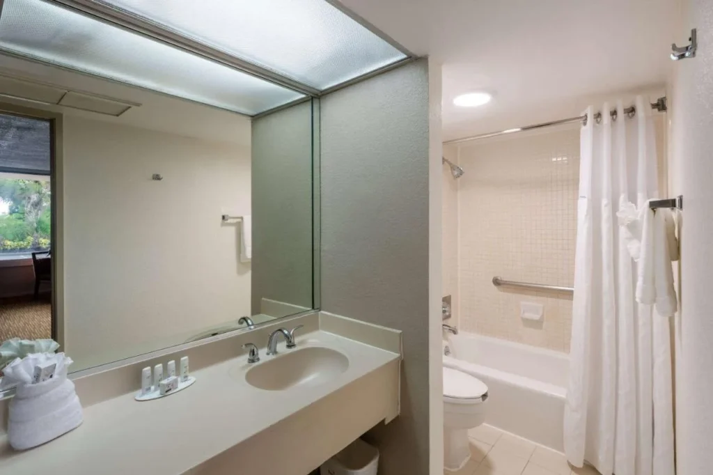 Cuarto de ba&ntilde;o con un tocador largo, espejo ancho y ba&ntilde;era-ducha en Ramada by Wyndham Kissimmee Gateway