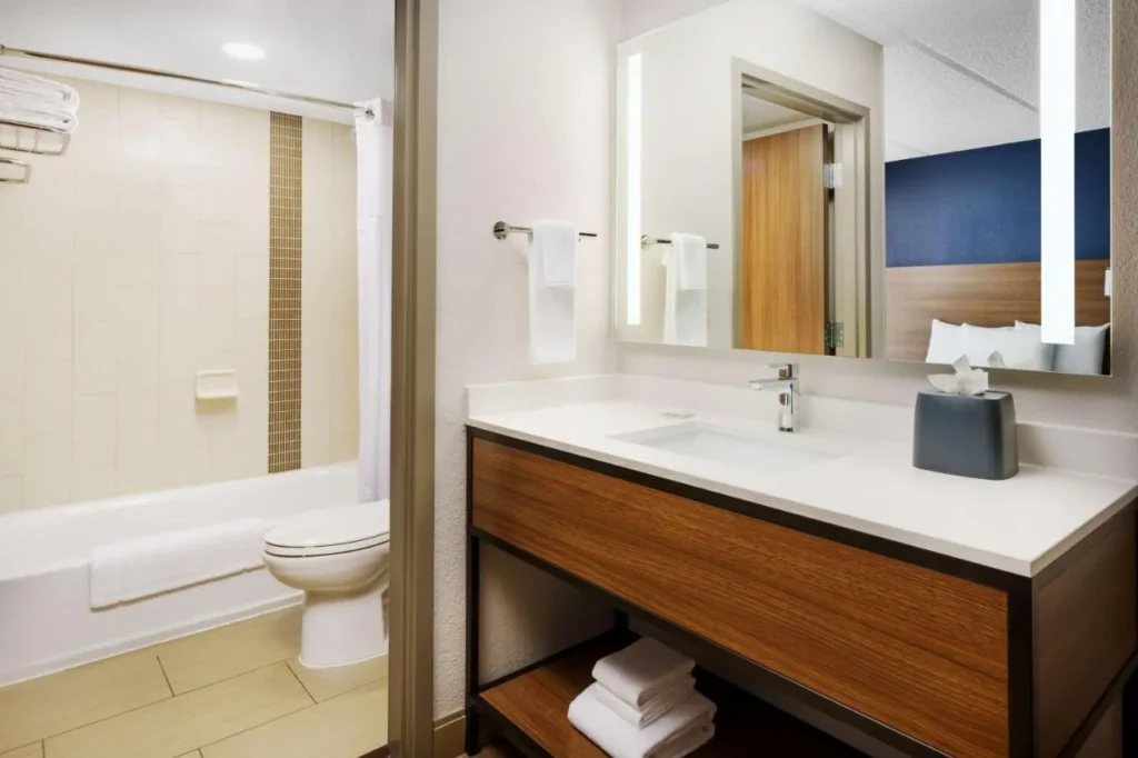 Cuarto de baño con ducha, inodoro y tocador de madera en Hyatt Place across from Universal