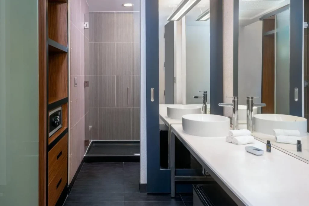 Cuarto de baño con lavabo, ducha con puerta de cristal y caja fuerte en la habitación en Aloft Orlando Downtown