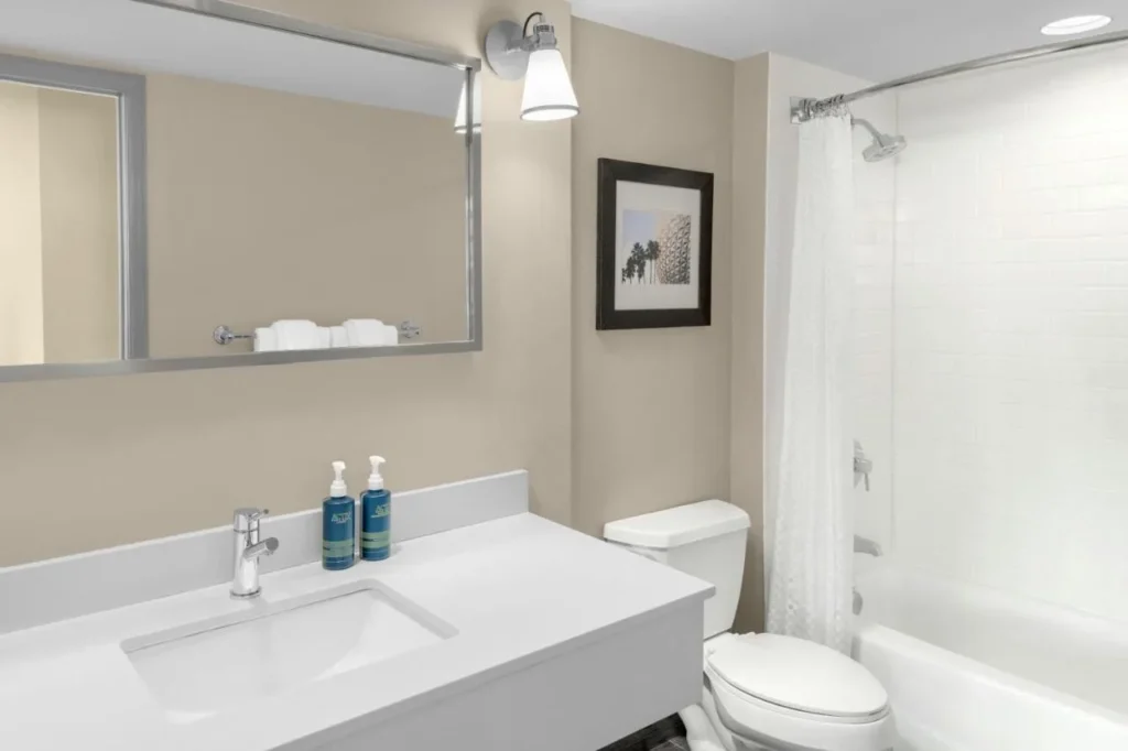 Cuarto de baño con tocador blanco, impresión enmarcada y combinación de ducha y bañera en Four Points Orlando International Drive