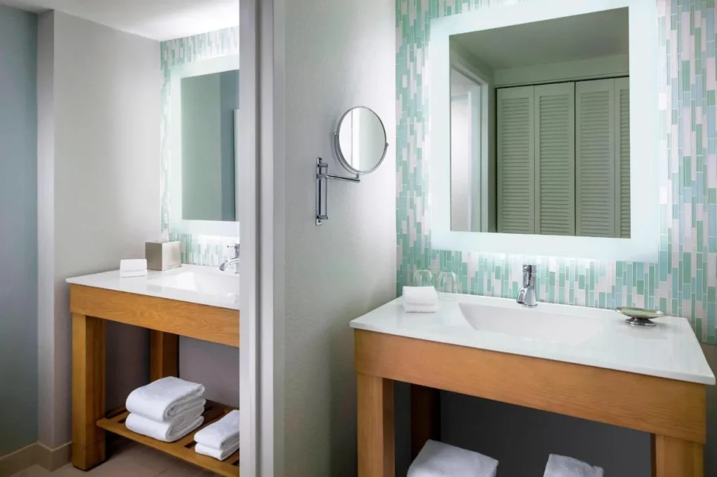Cuarto de ba&ntilde;o con tocador de madera, espejo retroiluminado y azulejos de vidrio en el Walt Disney World Swan