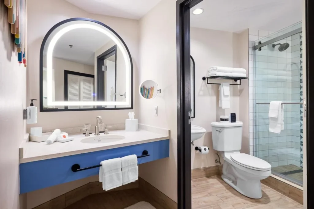 Cuarto de ba&ntilde;o con un espejo arqueado iluminado, tocador azul y ducha a ras de suelo en Hard Rock Hotel Orlando