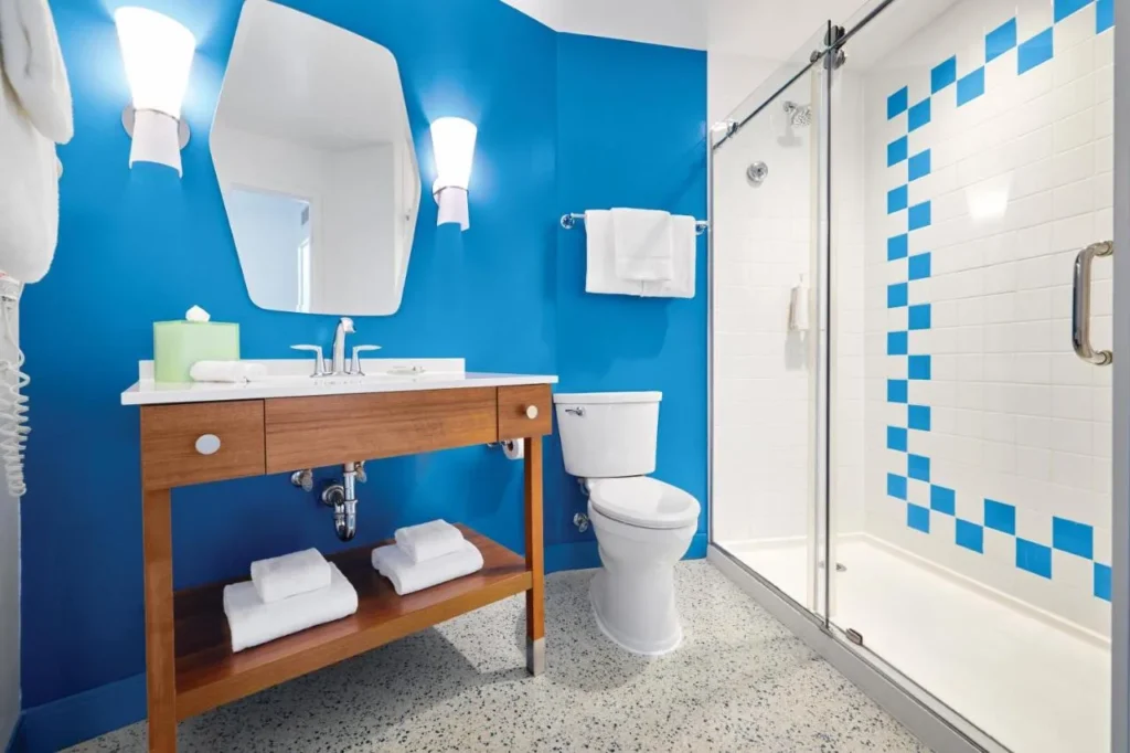 Cuarto de ba&ntilde;o con paredes azules, tocador de madera y cabina de ducha de cristal en Cabana Bay Beach Resort