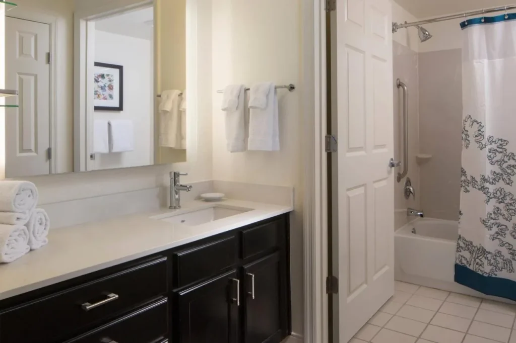 Cuarto de baño con tocador oscuro, espejo grande y combinación de ducha-bañera en el Residence Inn Orlando at SeaWorld