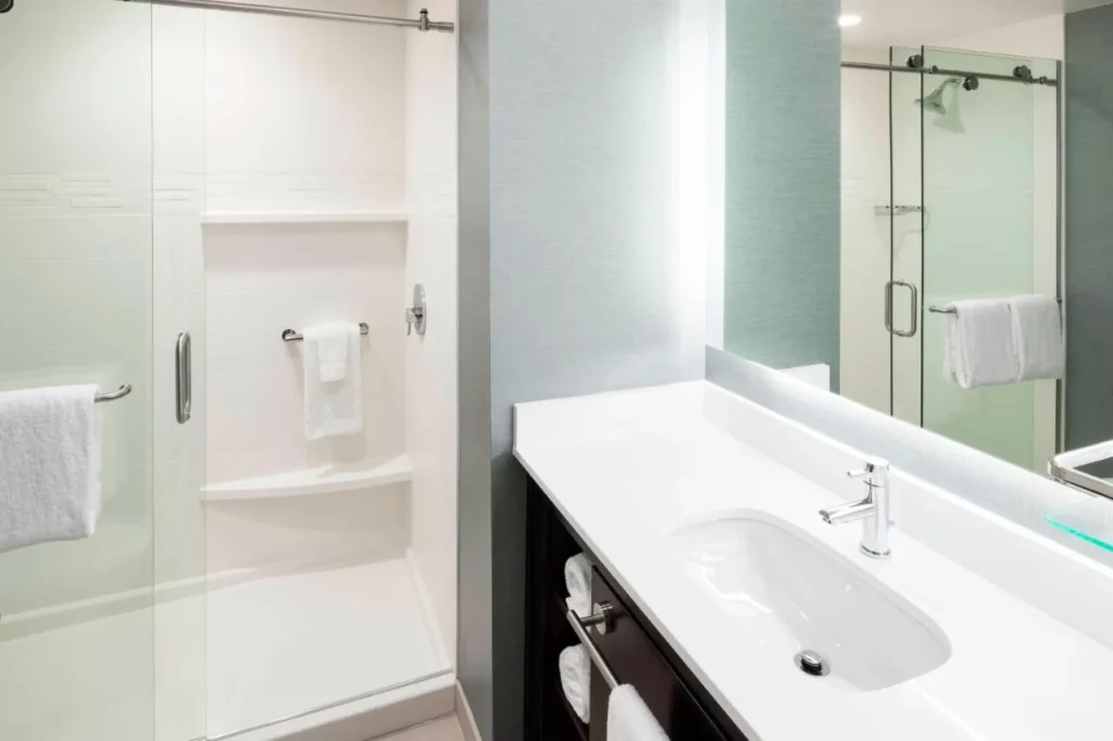 Cuarto de ba&ntilde;o con ducha a ras de suelo de cristal y tocador blanco en el Residence Inn Near Universal Orlando
