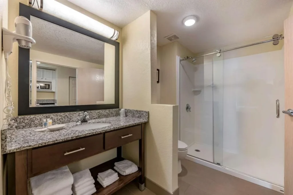 Cuarto de ba&ntilde;o con tocador de granito y ducha a ras de suelo de cristal en Comfort Suites Maingate East