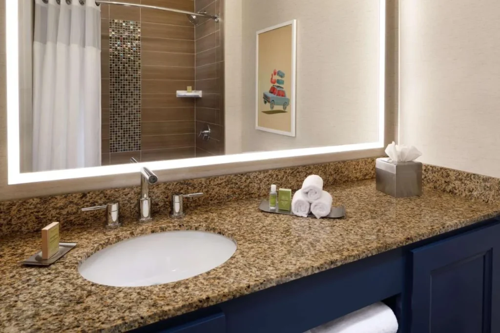 Cuarto de ba&ntilde;o con tocador de granito y espejo iluminado en una suite en DoubleTree Suites Disney Springs