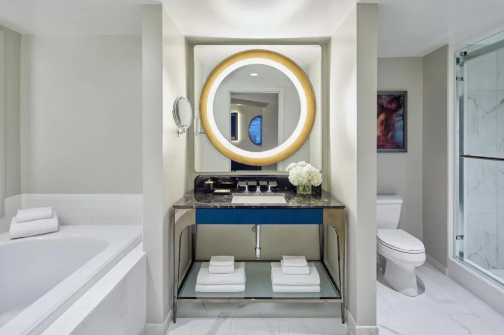 Bathroom with soaking tub, round lit mirror, vanity and glass shower at Hotel Beauden