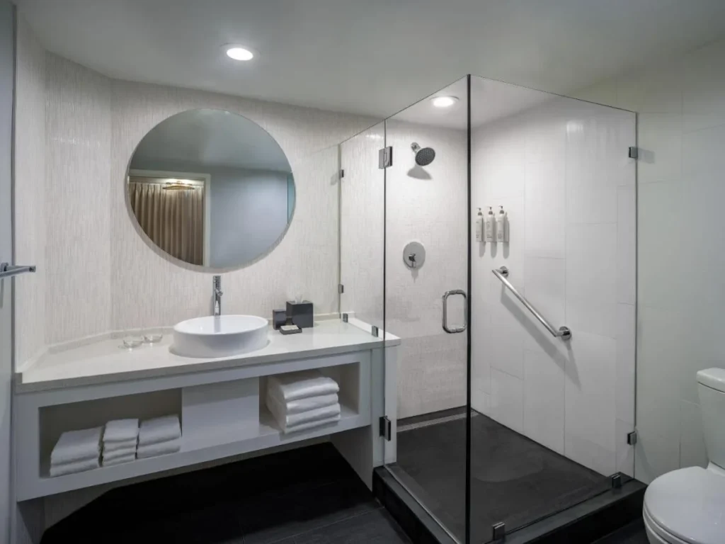 Cuarto de baño con lavabo, espejo redondo y ducha a ras de suelo de cristal en Renaissance Orlando Resort