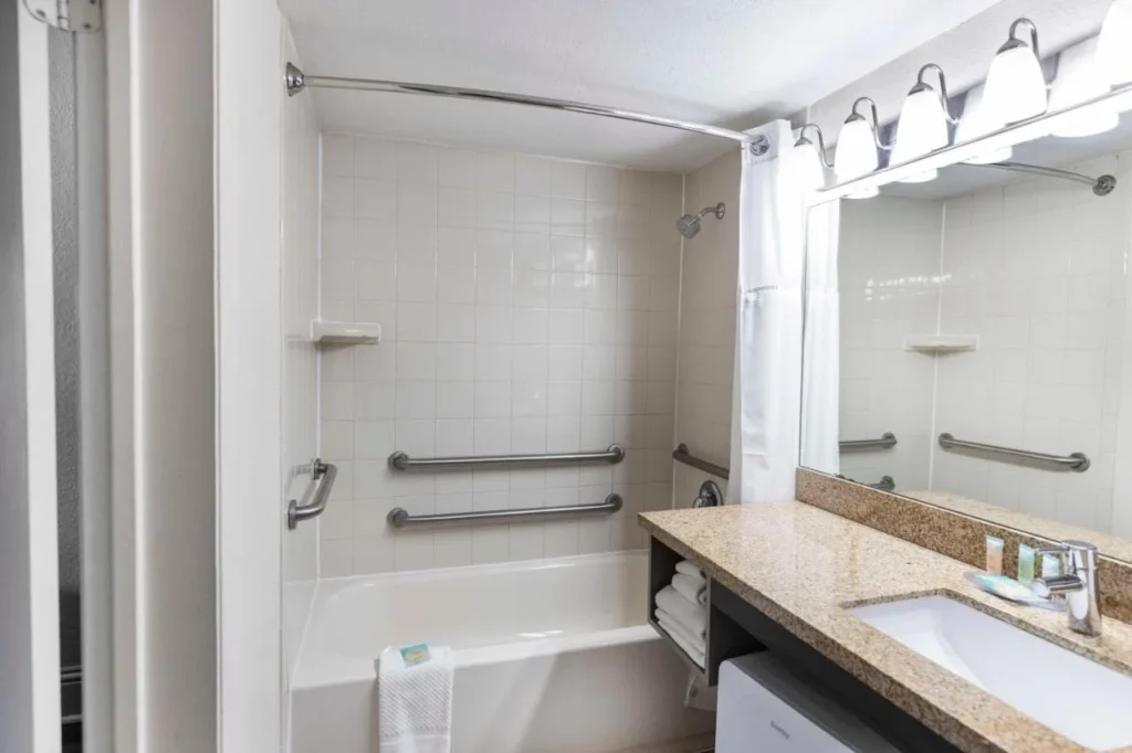 Bañera con barras de apoyo y tocador de granito en un baño accesible en Avanti International Resort