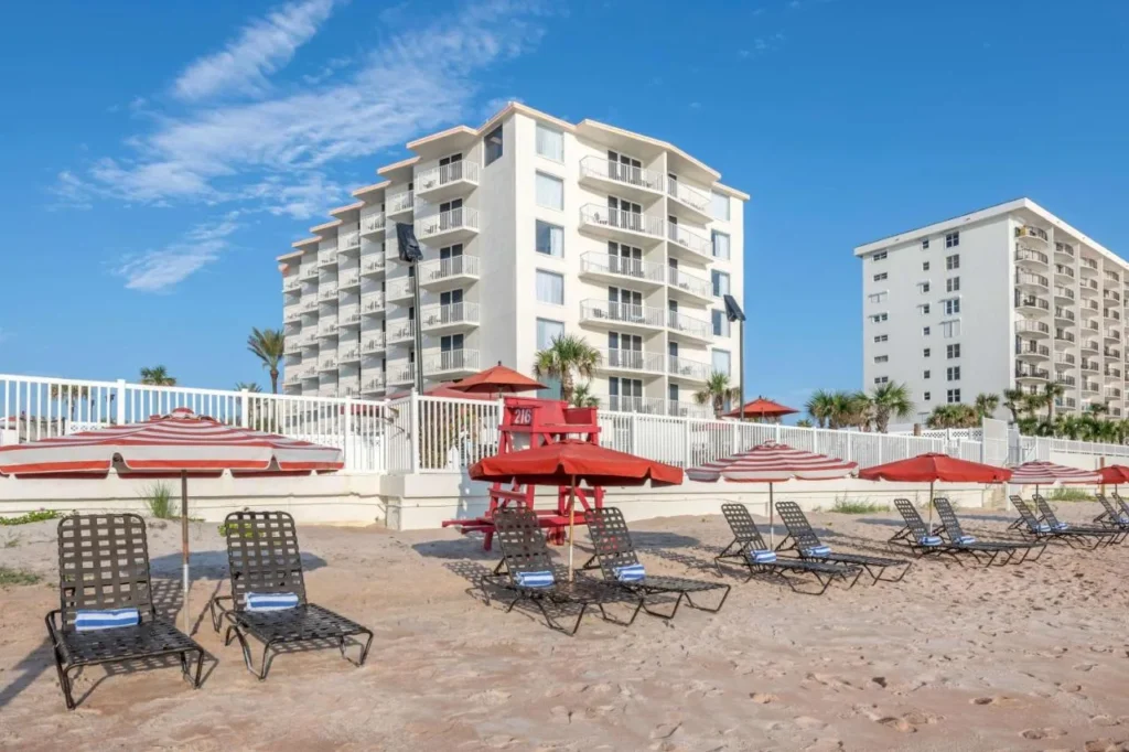 Tumbonas de playa y sombrillas rojas debajo de la torre del condominio en The Cove en Ormond Beach
