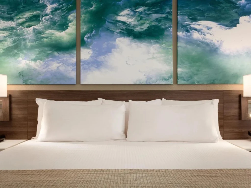 Cama con almohadas blancas bajo una gran pintura de tres paneles en Buena Vista Suites