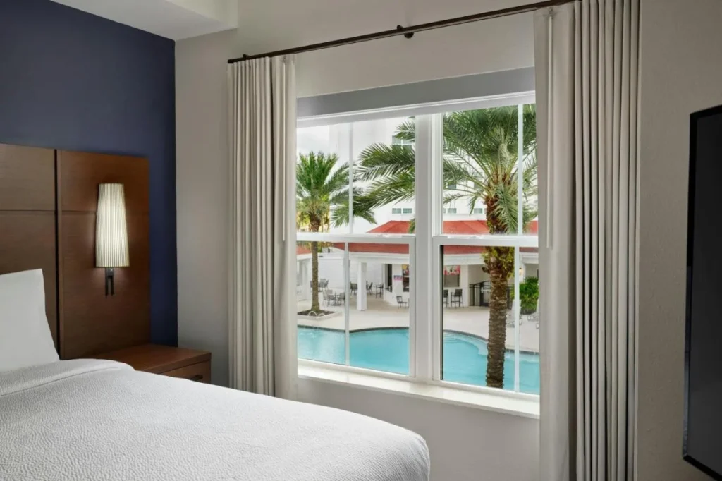 Ventana del dormitorio con vistas a la piscina y las palmeras en el Residence Inn Orlando at Flamingo Crossings