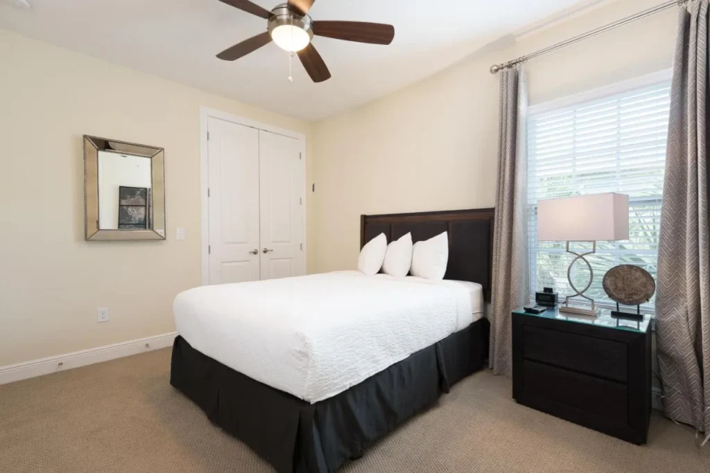 Dormitorio con cabecero oscuro, ropa de cama blanca y ventilador de techo en una casa de Encore Resort